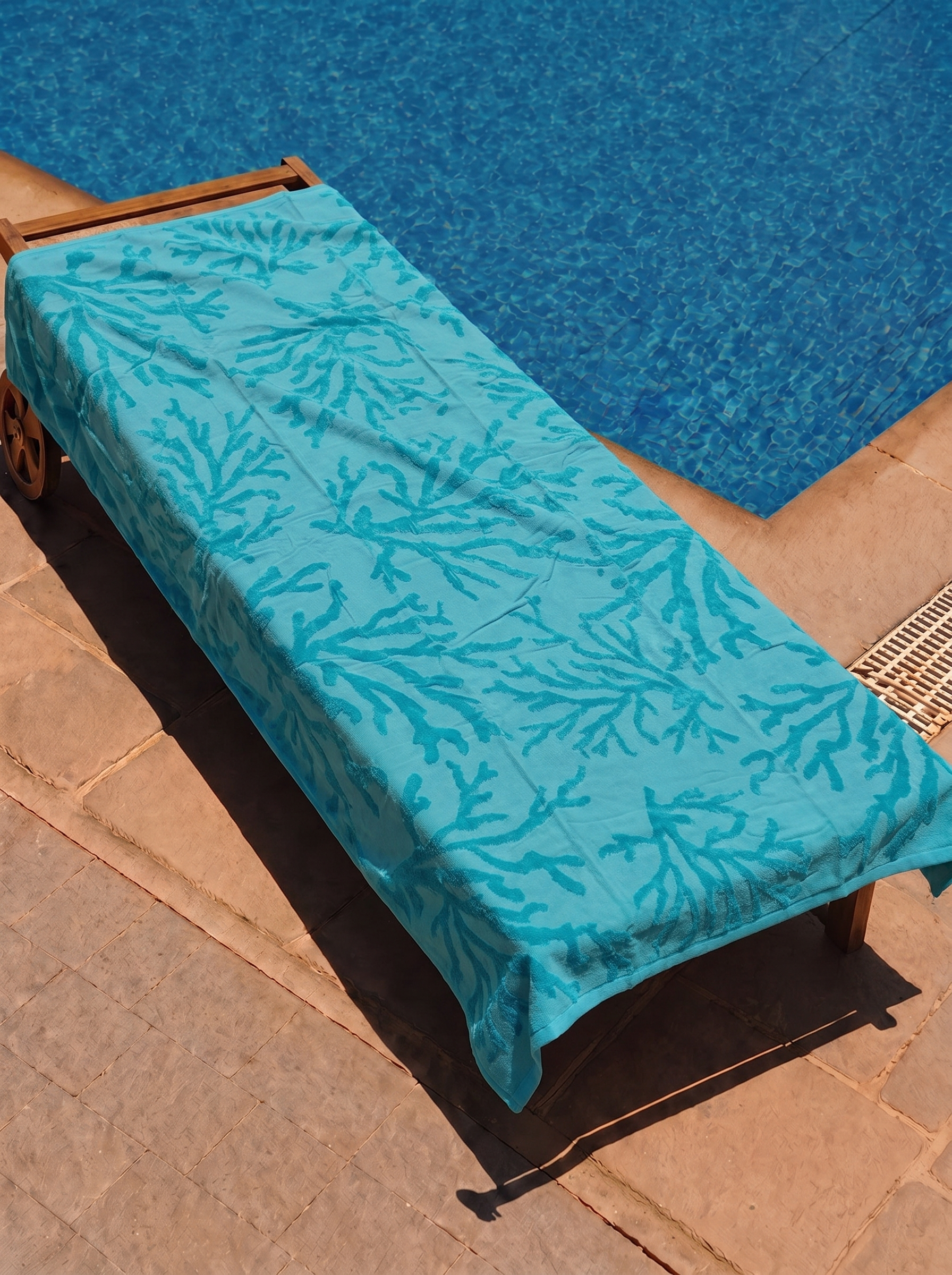 Teal tonal coral branch towel on a poolside lounge chair