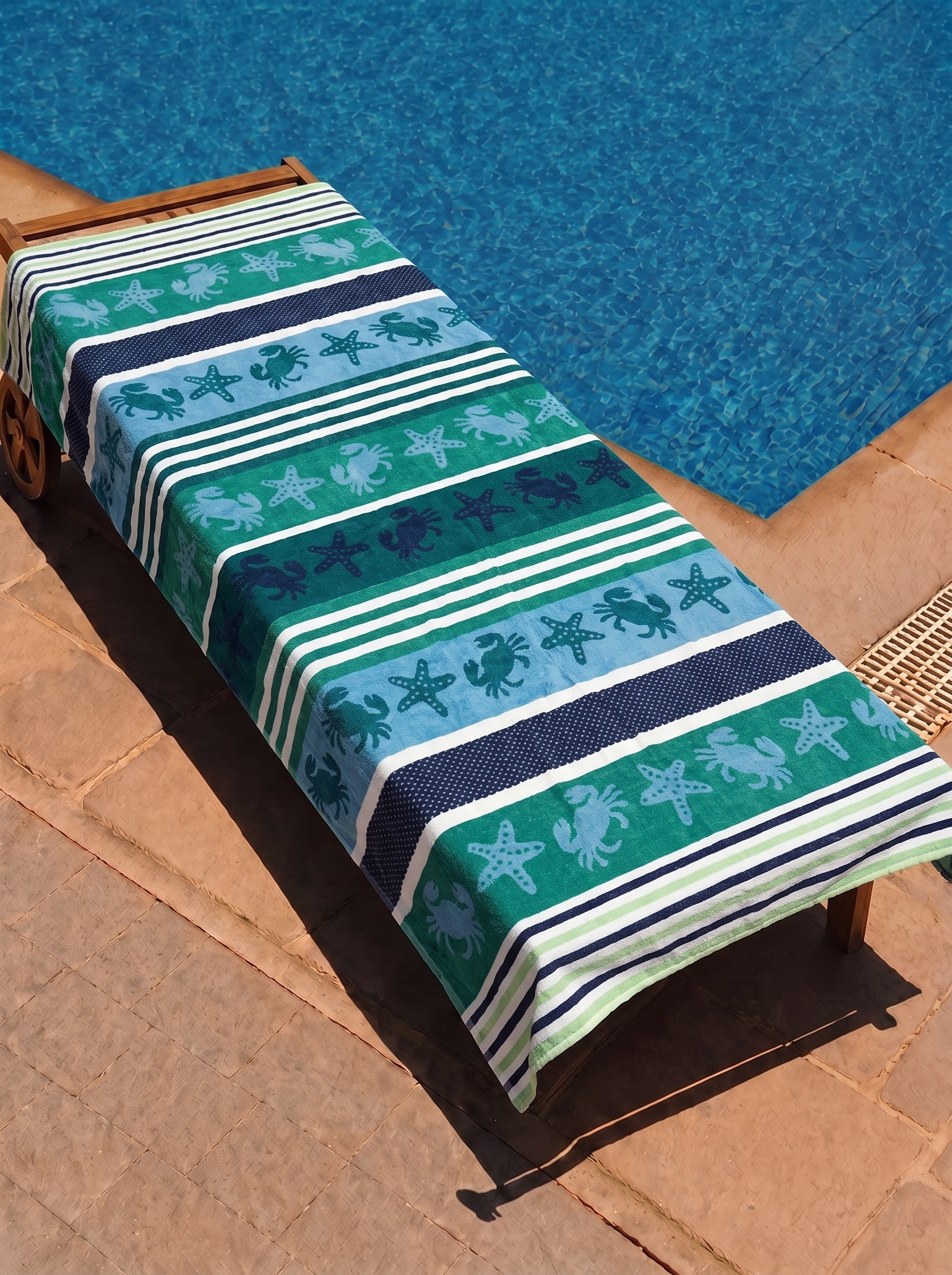Green and blue crab and starfish stripe towel on a poolside lounge chair