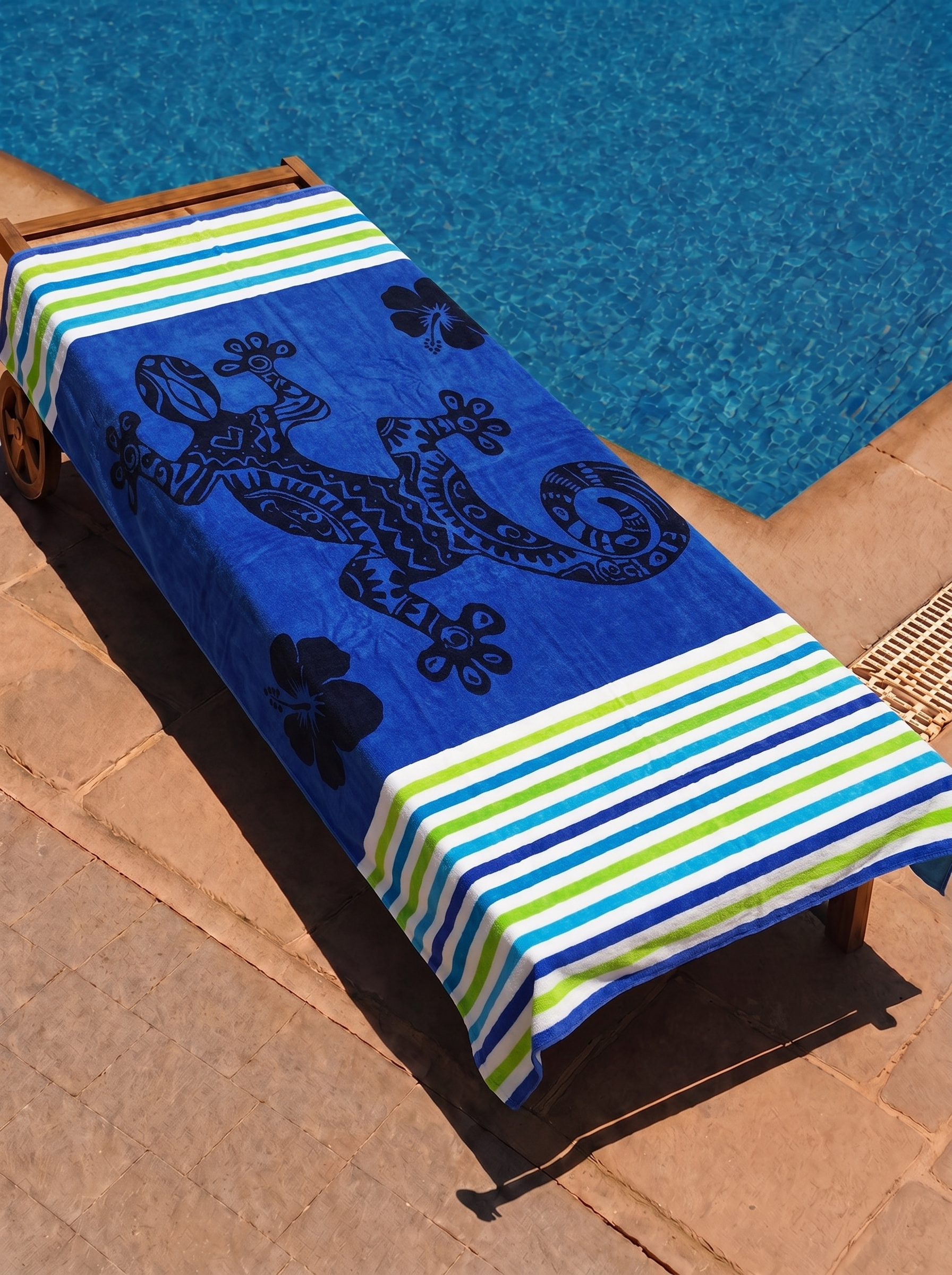 Blue gecko and hibiscus stripe towel on a poolside lounge chair
