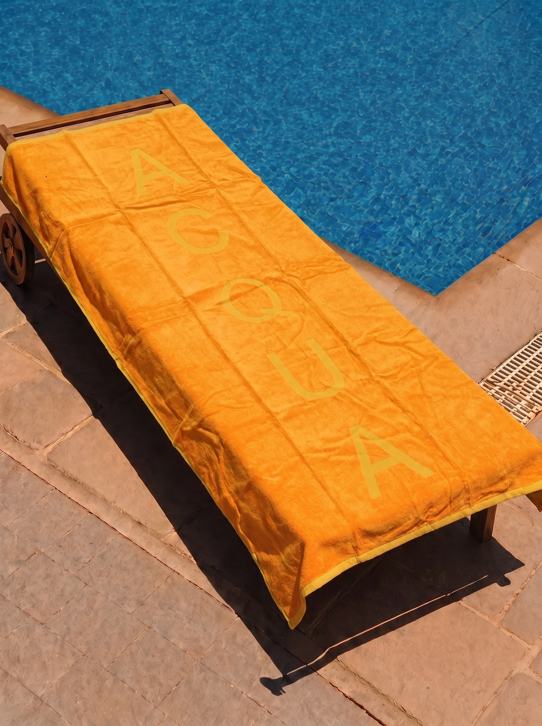 Orange Acqua text towel on a poolside lounge chair