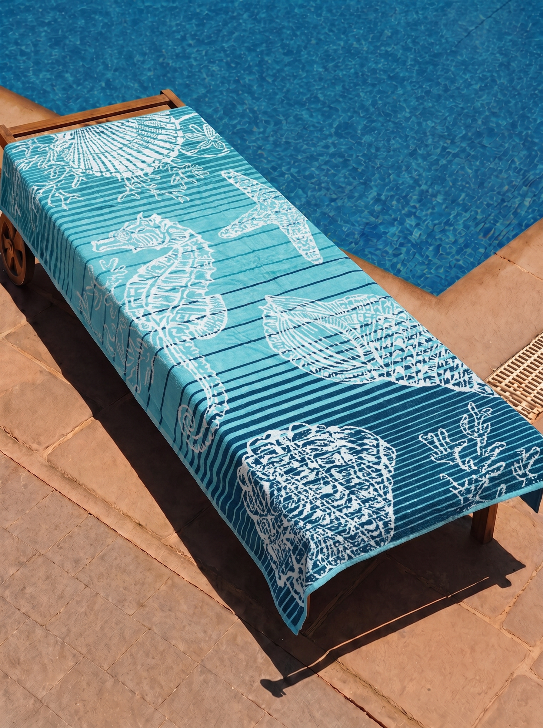 Teal seahorse and shell ombre towel on a poolside lounge chair