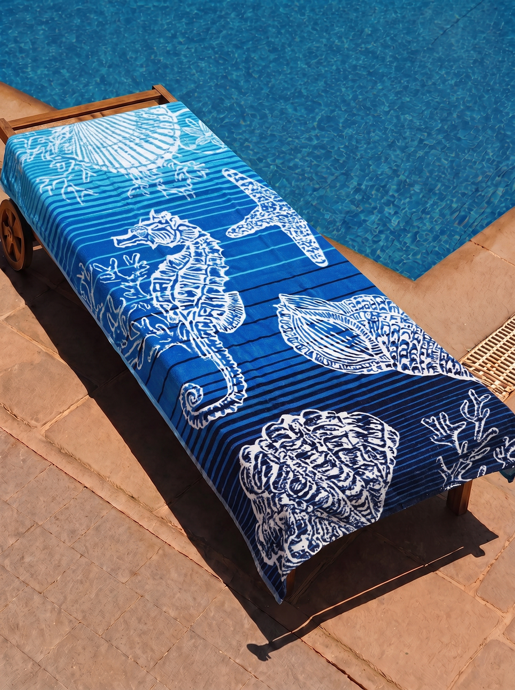 Deep blue seahorse and shell ombre towel on a poolside lounge chair